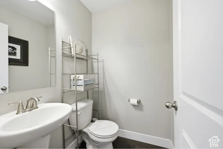 Pedestal sink with brushed nickel faucet, wall-mounted mirror, white paneled door, and dark wood-finish flooring