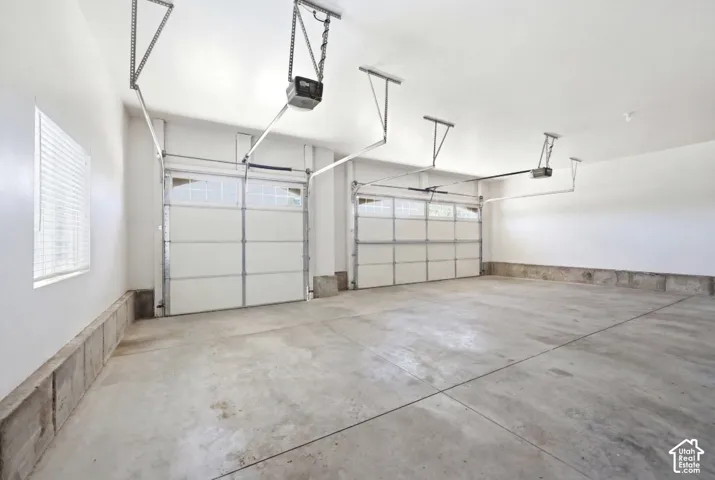 Two-car garage with concrete flooring, two automatic garage door openers, and a window with horizontal blinds