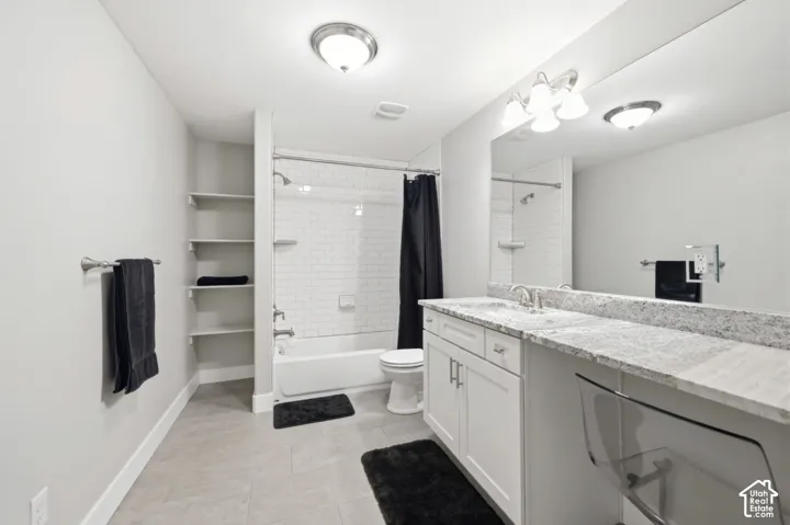 Modern bathroom featuring a double vanity with stone countertops, white shaker cabinetry, an integrated rectangular sink, and a tiled shower-tub combination
