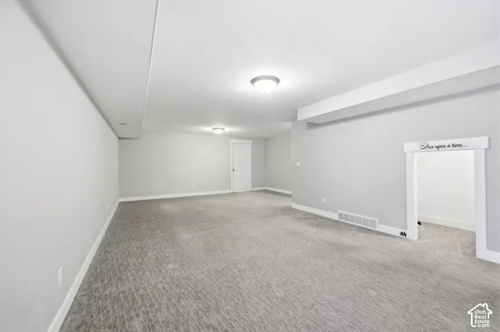Spacious room featuring light gray carpeting, overhead flush-mount lighting, and neutral wall tones