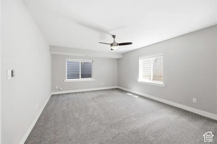 Neutral wall paint, gray carpeting, dual windows, and a ceiling fan with integrated lighting