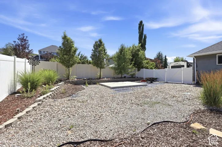 Expansive gravel backyard featuring a concrete pad, white vinyl fencing, and established perimeter landscaping