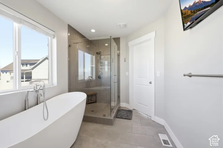 Freestanding soaking tub with chrome fixtures, glass-enclosed shower with tile surround, and light gray floor tiles