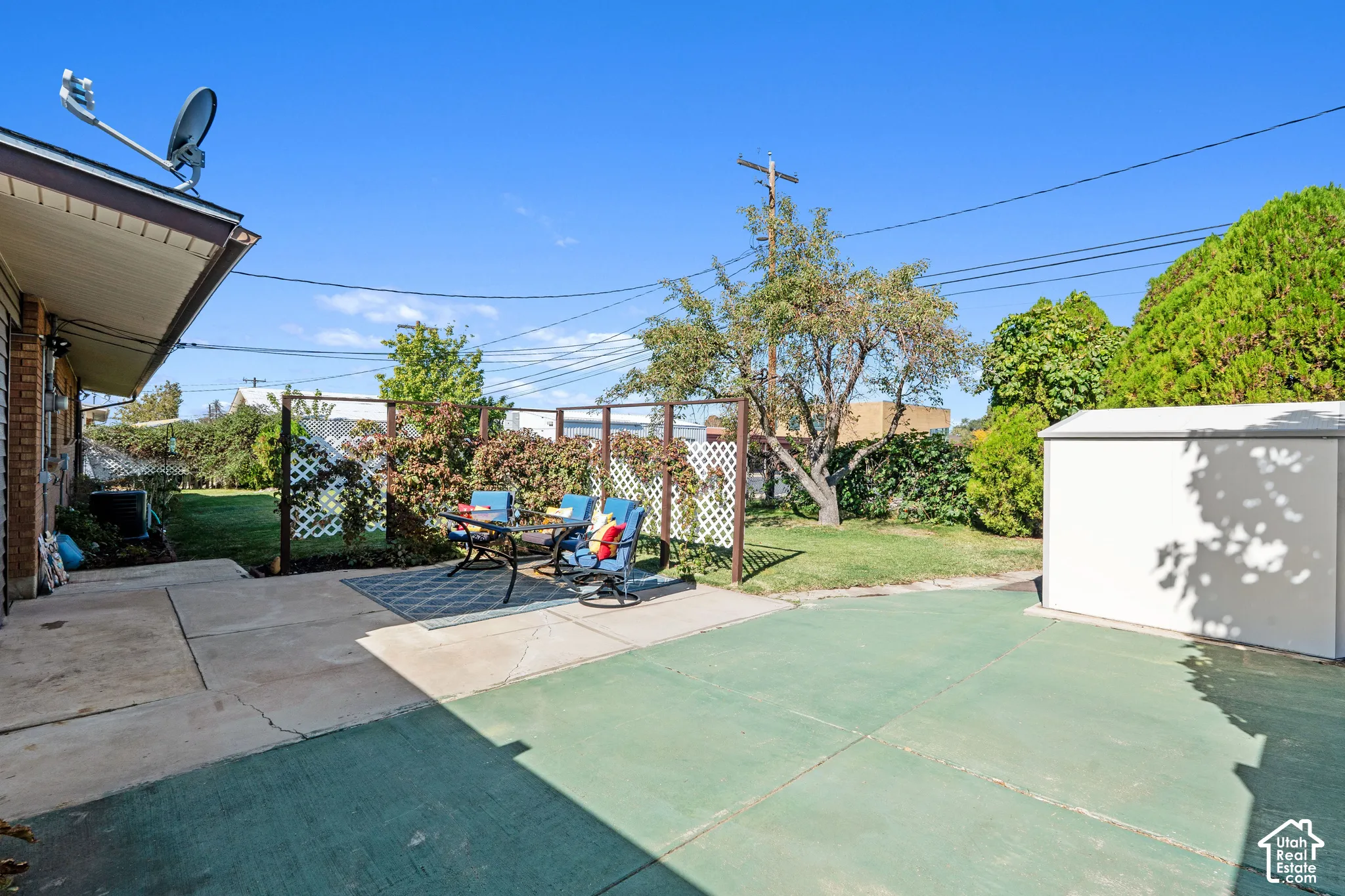 Expansive backyard featuring a concrete patio, a green-painted concrete area, a white storage shed, and mature landscaping