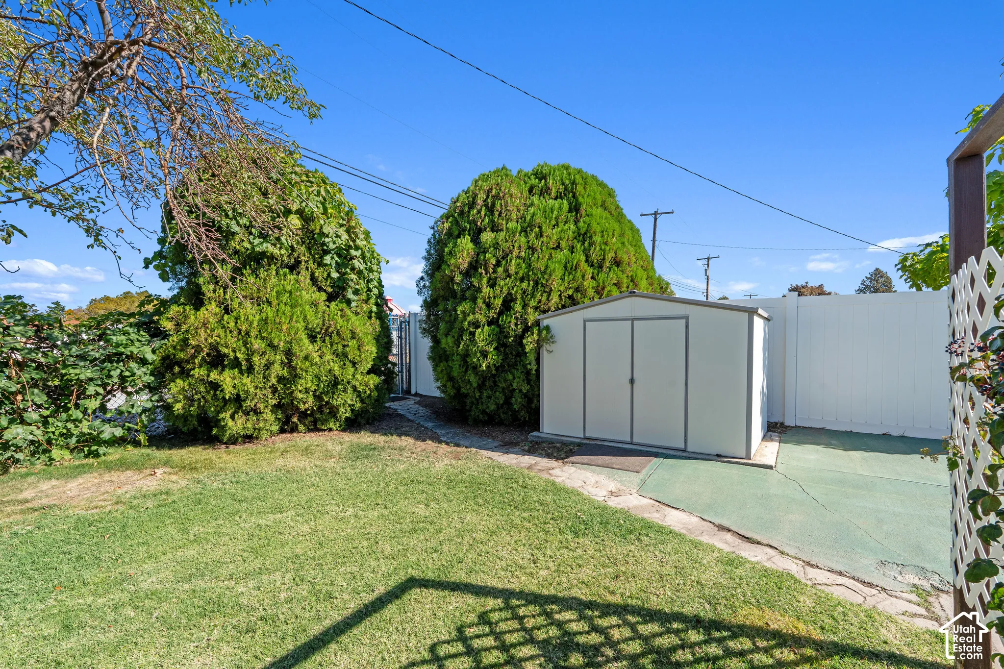 Expansive backyard featuring a manicured lawn, established shrubs, a white privacy fence, and a modern metal storage shed