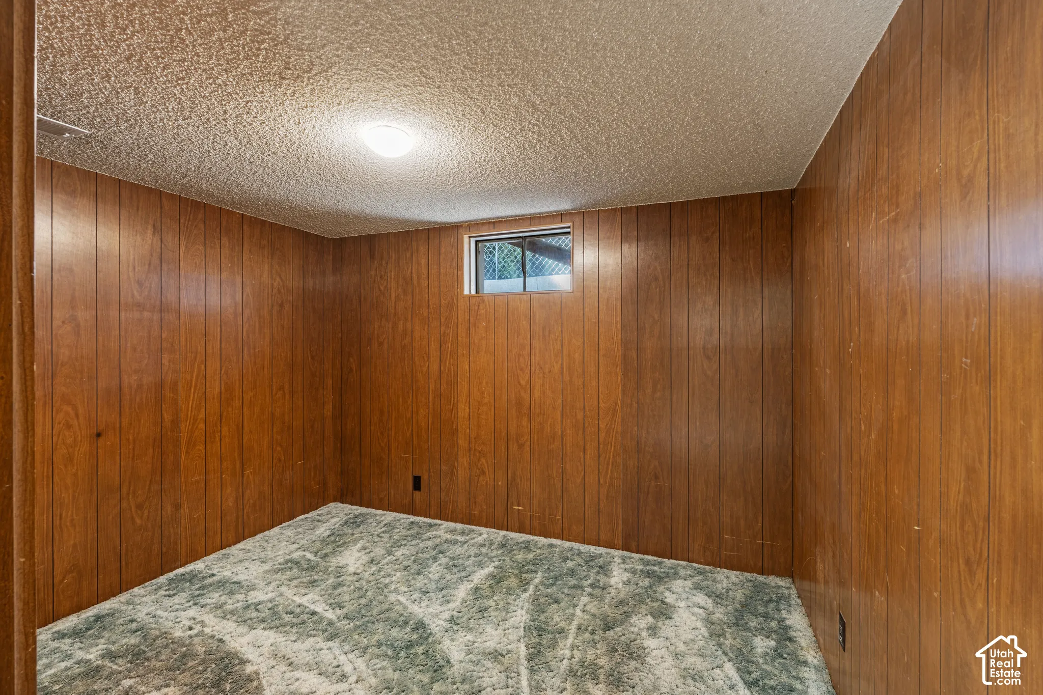 Room featuring wood-paneled walls, a single window, and a textured ceiling