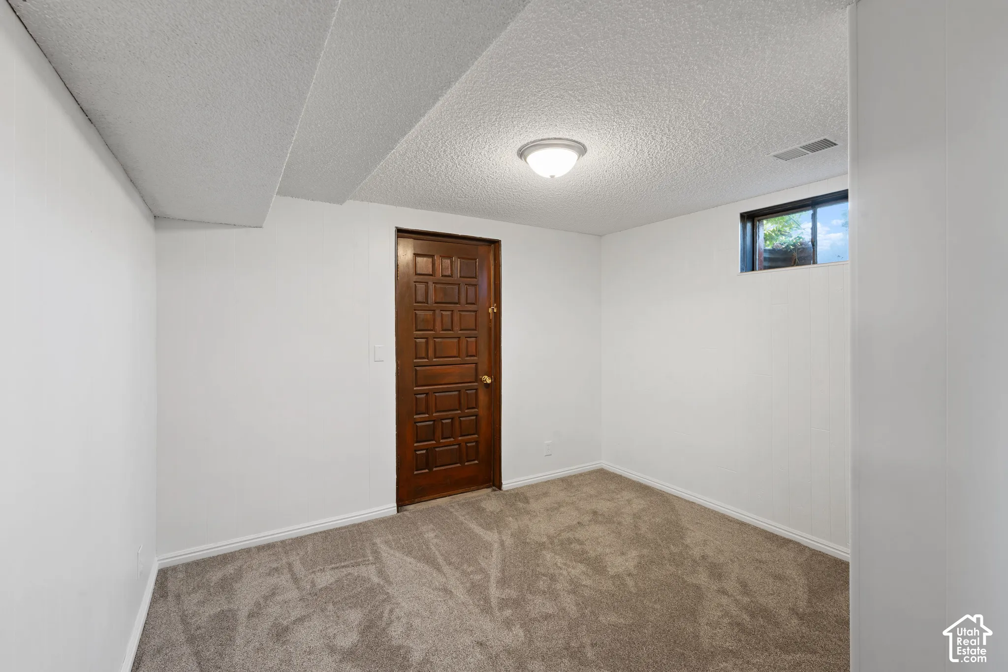 Recessed window, textured ceiling, flush mount lighting, dark wood-finish door, and neutral-tone carpeting