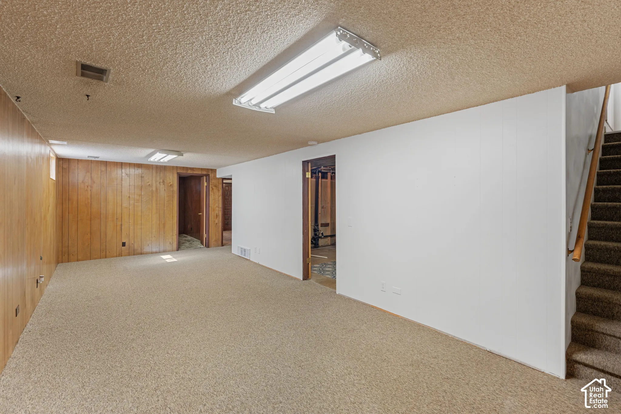 Carpeted flooring extending throughout, paneled wall detailing, white painted wall, integrated lighting fixtures, and carpeted staircase with a wood handrail