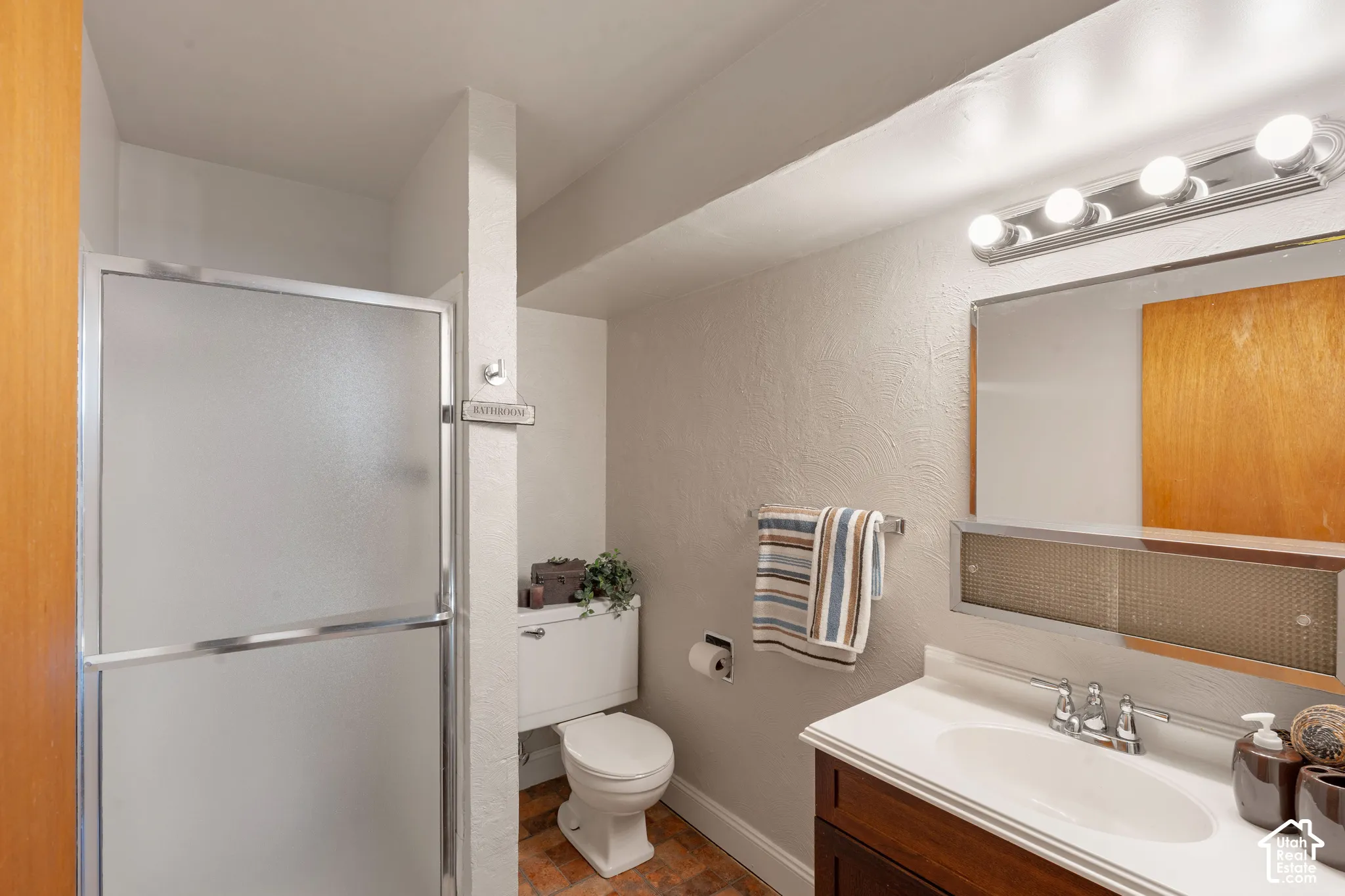 Shower enclosure with frosted glass panels, single vanity with integrated sink, wood-finish cabinetry, and vanity light fixture