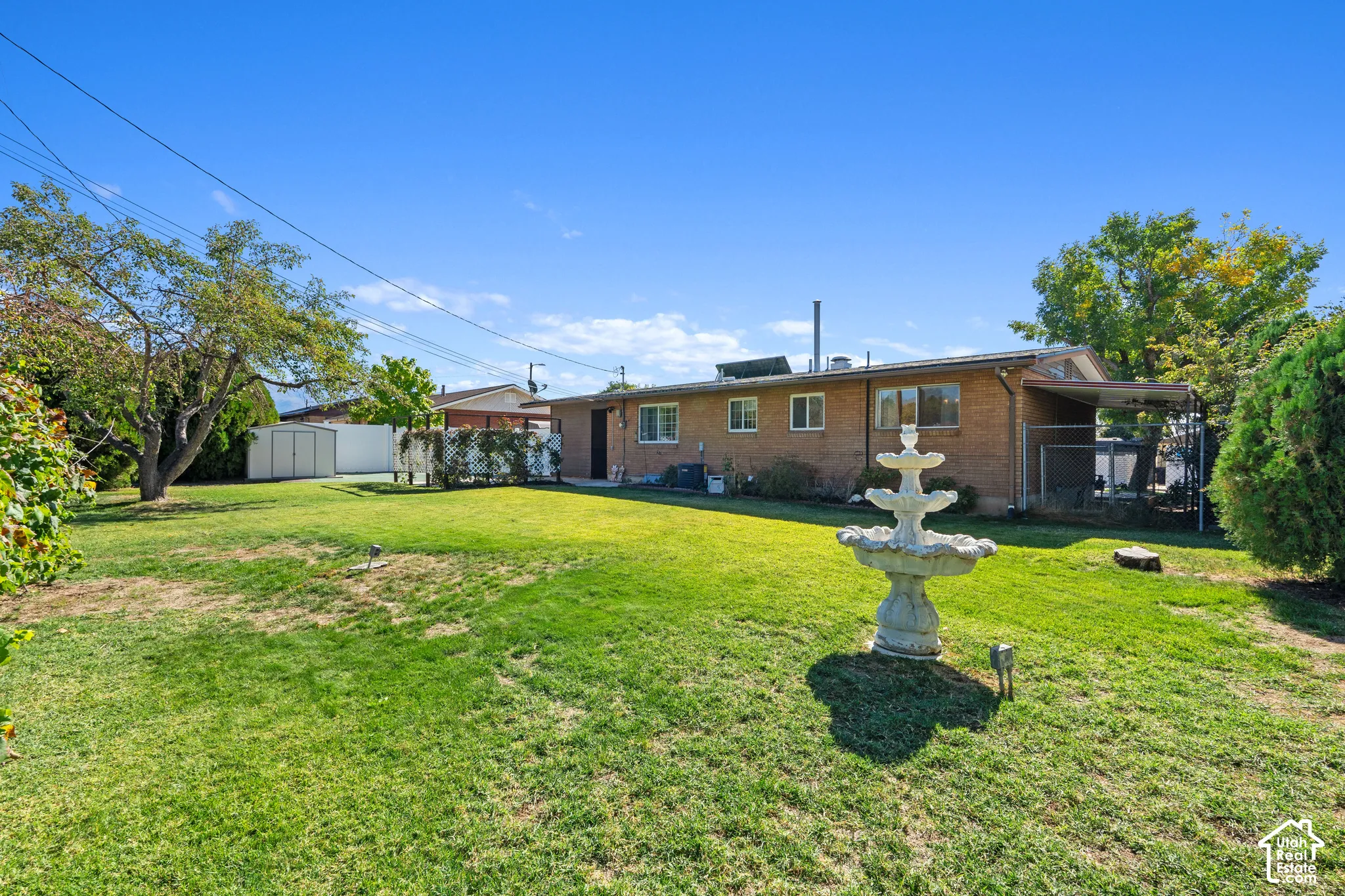 Expansive green lawn featuring a three-tiered fountain, mature trees, and a brick exterior with multiple windows