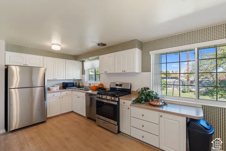 White cabinetry, stainless steel appliances, wood-finish flooring, light-toned countertops, and a large window