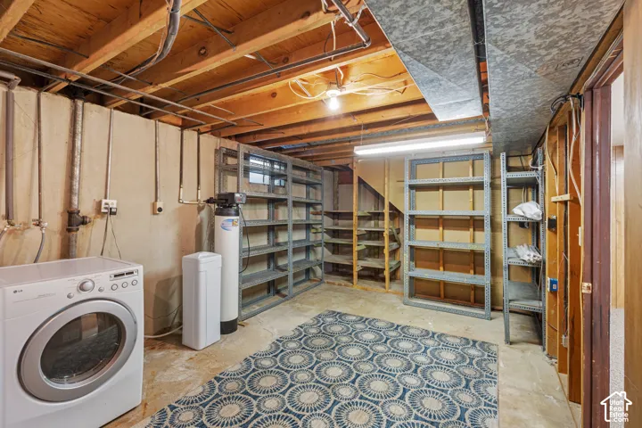 Unfinished basement featuring exposed wood joists, concrete foundation walls, and metal storage shelving