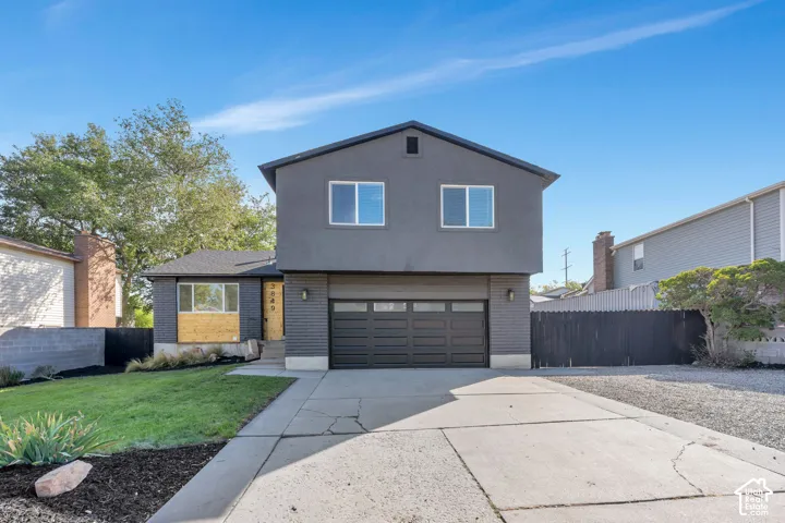 Two-story facade with a dark gray finish, featuring a prominent garage door, a concrete driveway, and a manicured lawn