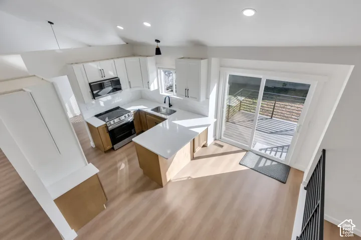 Vaulted ceilings enhance this kitchen featuring white cabinetry, stainless steel appliances, and light wood-finish flooring