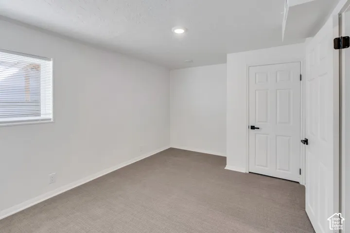 Recessed lighting illuminating a room with neutral-toned carpeting, white walls, and a window with blinds