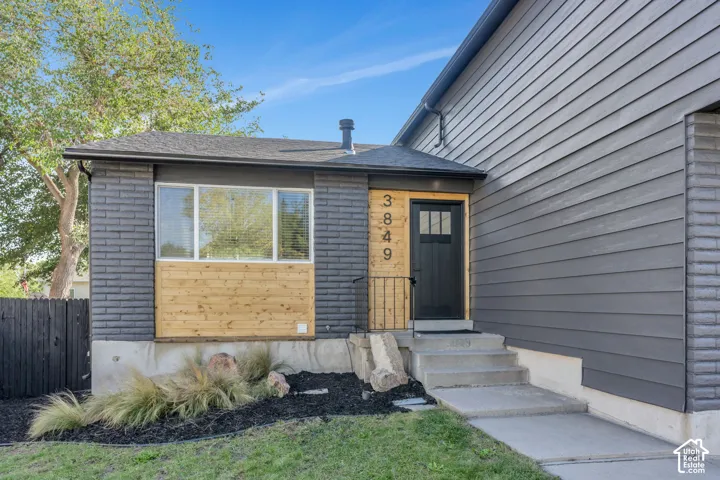 Exterior featuring contrasting horizontal siding and brickwork, a dark entry door with glass panels, concrete steps, and integrated landscaping with decorative rocks