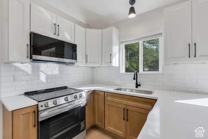 White shaker-style upper cabinetry with dark hardware, a stainless steel range with an overhead microwave, white subway tile backsplash, and light-toned countertops