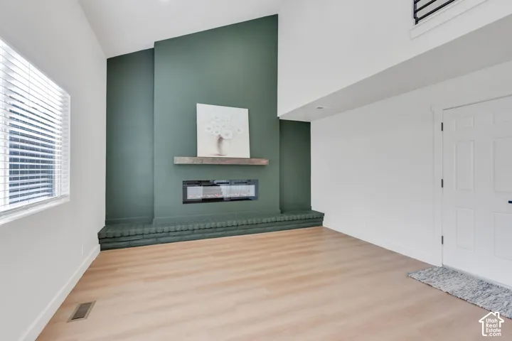 Vaulted ceiling, wood-finish flooring, accent wall, modern electric fireplace with wood mantel, and white interior doors