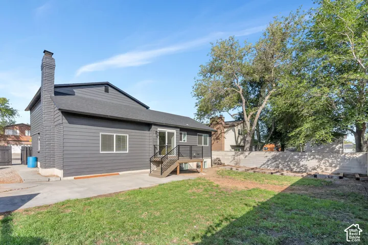 Rear exterior featuring dark horizontal siding, a substantial chimney, a rear deck with dark railings, and a concrete patio