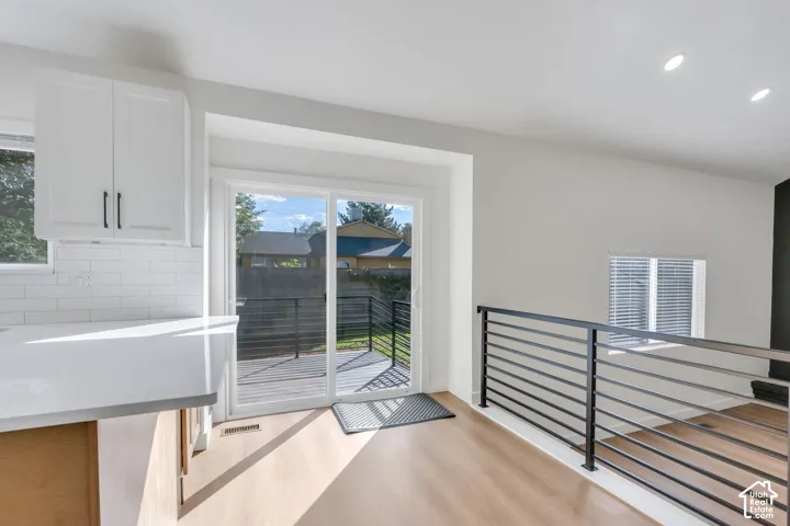 White shaker cabinetry, subway tile backsplash, sliding glass door, wood-finish flooring, and a modern horizontal railing