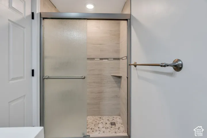 Shower enclosure with textured glass sliding doors, tiled walls, a built-in corner shelf, recessed lighting, and a pebble-finish shower floor