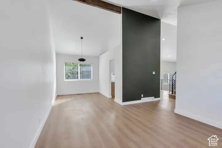 Vaulted ceilings with an exposed wood beam, wood-finish flooring, a contemporary pendant light fixture, and a dark accent wall