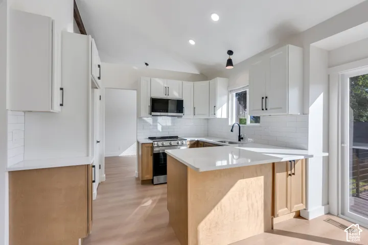 Vaulted ceiling kitchen featuring white shaker cabinetry, an island with stone countertops, stainless steel appliances, and a subway tile backsplash