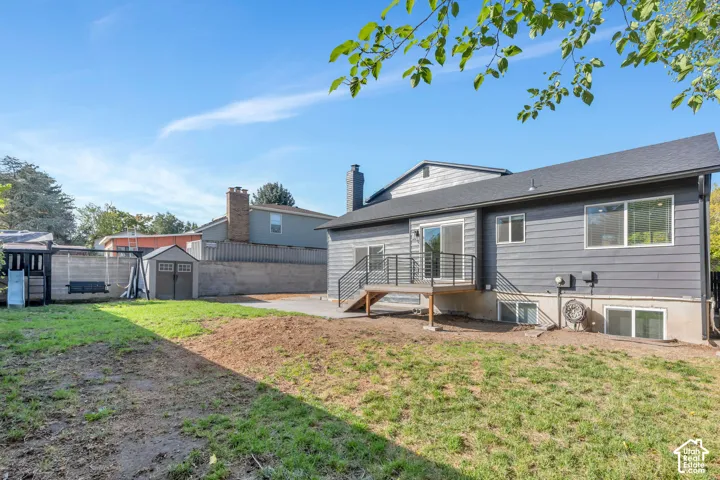Rear exterior with gray siding, a deck with black railing, a ground-level patio, and multiple windows