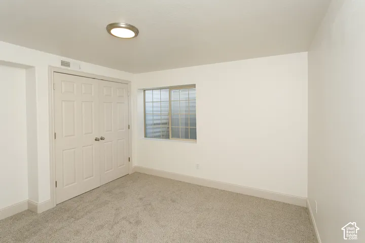 Recessed window with security bars, light-colored carpeting, white interior walls, overhead flush mount lighting, and bi-fold closet doors