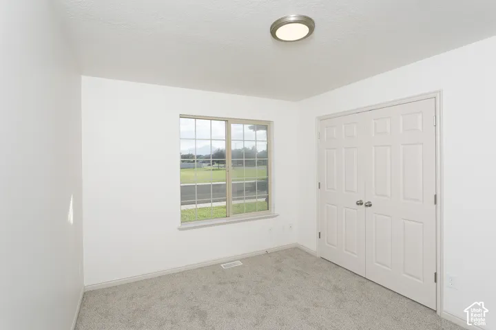 Recessed window with grid pattern, neutral carpet, bi-fold closet doors, and flush-mount ceiling light