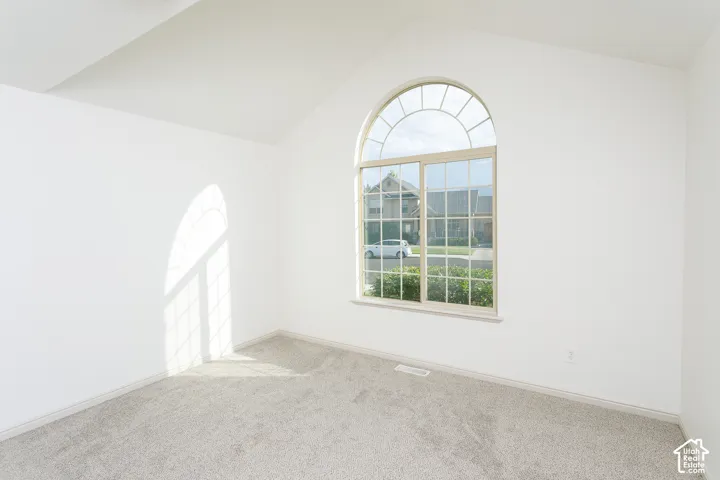 Arched window with gridded panes, vaulted ceiling, neutral wall finish, and carpeted flooring