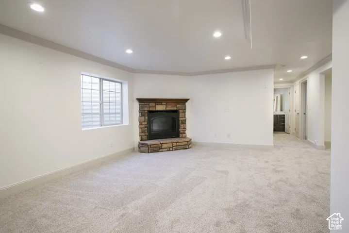 Recessed lighting illuminating plush carpeting and a stone-faced fireplace with a wood mantle