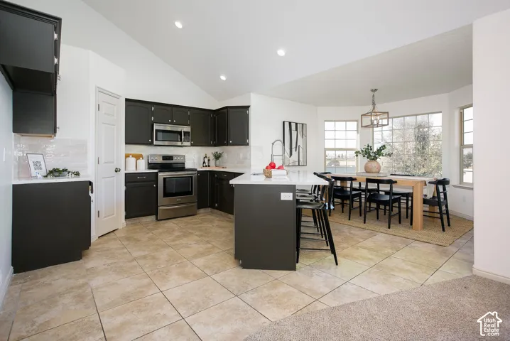 Kitchen featuring dark cabinetry, stainless steel appliances, a center island with seating, and bay windows