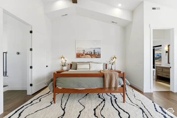 Vaulted ceiling with exposed beam, recessed lighting, wood-finish flooring, and a white interior door with black hardware