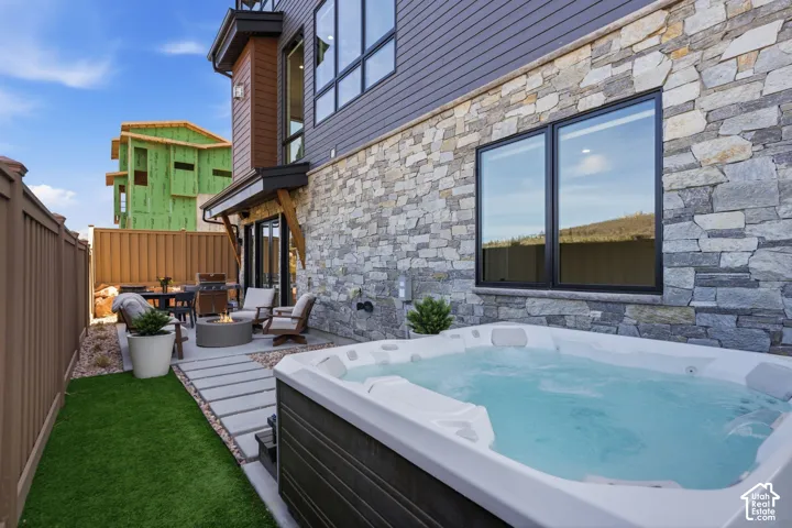 Private patio featuring a hot tub, artificial turf, stone wall facade, wood-clad siding, and large black-framed windows