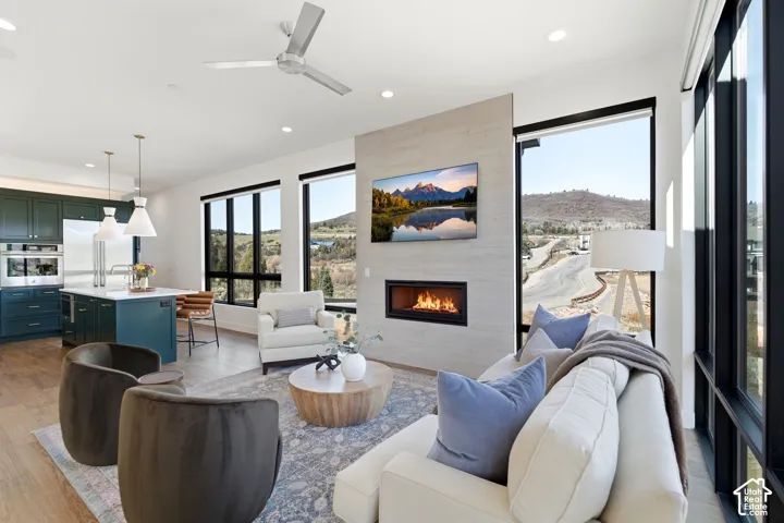 Open-concept living space anchored by a linear gas fireplace with stone surround, complemented by large black-framed glass doors and windows flooding the area with natural light