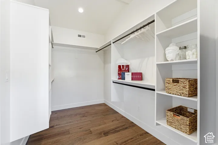 Wood-finish flooring, built-in shelving, hanging rods, recessed lighting, and a vaulted ceiling