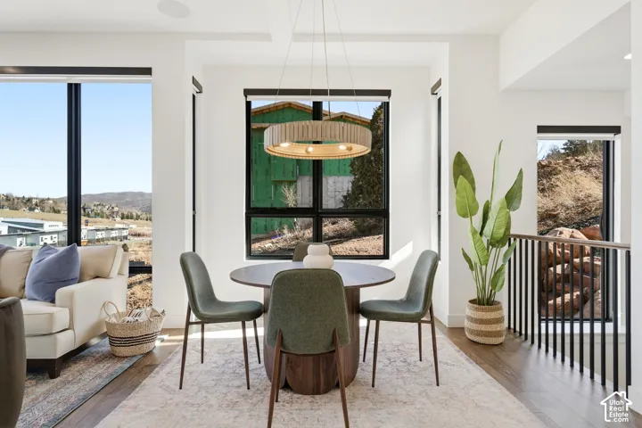 Modern dining area anchored by a round wood-finish table and upholstered chairs, illuminated by a contemporary pendant fixture