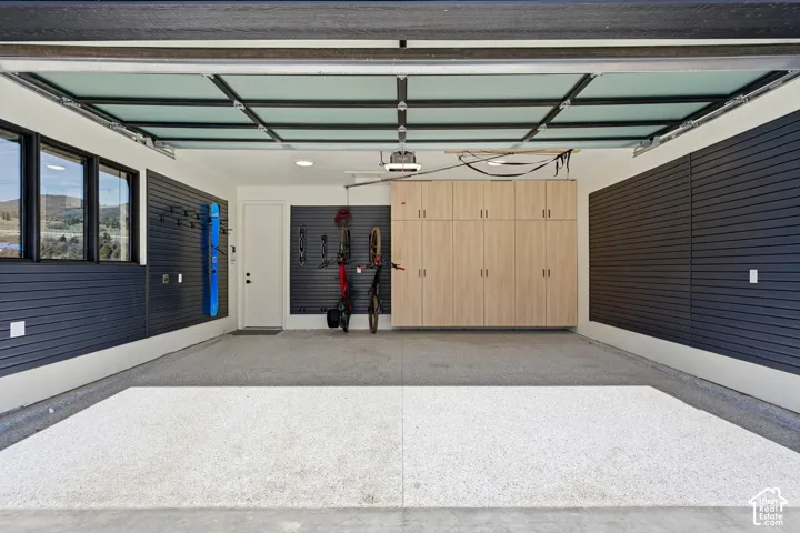 Garage featuring a light-toned epoxy floor, dark slatwall panels, built-in cabinetry, and multiple windows