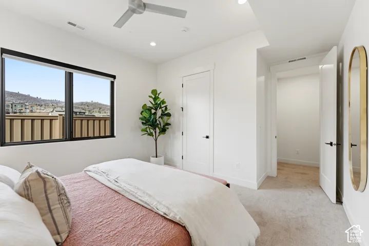 Bright primary bedroom featuring expansive windows with mountain and neighborhood views, neutral wall finishes, ceiling fan, recessed lighting, engineered wood-finish flooring, and direct access to a hallway leading to additional rooms and a round mirror
