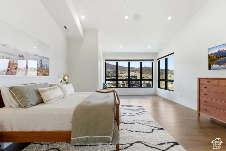 Spacious primary bedroom suite featuring hardwood flooring, recessed ceiling lights, and expansive multi-panel windows framing panoramic landscape vistas