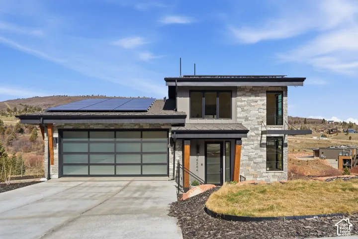 Contemporary architecture featuring stone and siding exterior, expansive windows, a translucent panel garage door, and rooftop solar panels