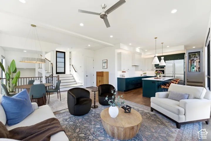 Open-concept living space featuring wood-finish flooring, a modern kitchen with a large island and dual pendant lighting, and a dining area with a linear chandelier