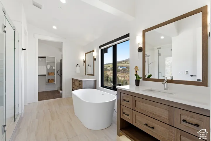 Freestanding soaking tub, dual vanities with wood-finish cabinetry, frameless glass shower enclosure, and large window with mountain scenery