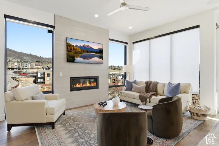 Contemporary living room featuring a linear gas fireplace with stone surround, expansive windows with motorized shades, wood-finish flooring, and recessed ceiling lighting