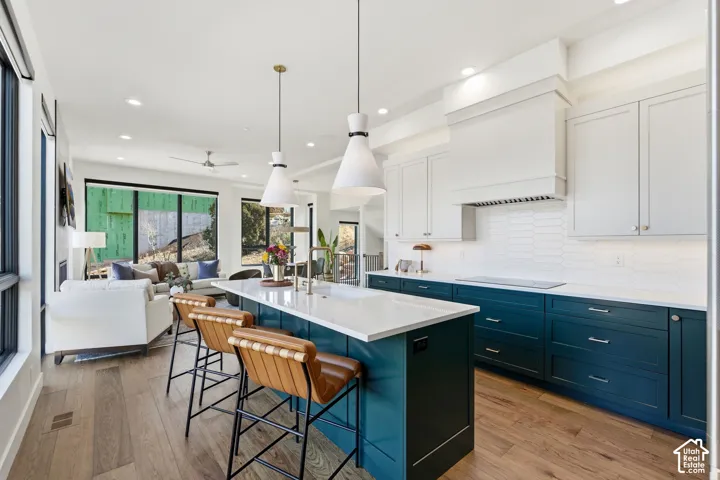 Contemporary kitchen and dining space featuring a two-tone cabinetry design with deep teal lower cabinets and white upper cabinetry, white quartz countertops, and a large waterfall-edge island with seating for three