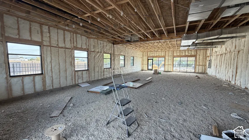 Exposed wood ceiling joists and beams, spray foam insulation on walls, multiple black-framed windows, and large glass panel doors