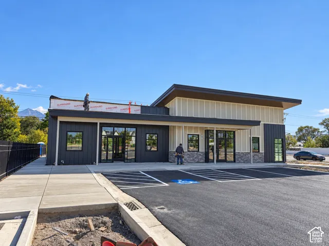 Contemporary commercial building with a black and light-toned vertical siding facade, large window panels, a covered entrance, and an asphalt parking lot