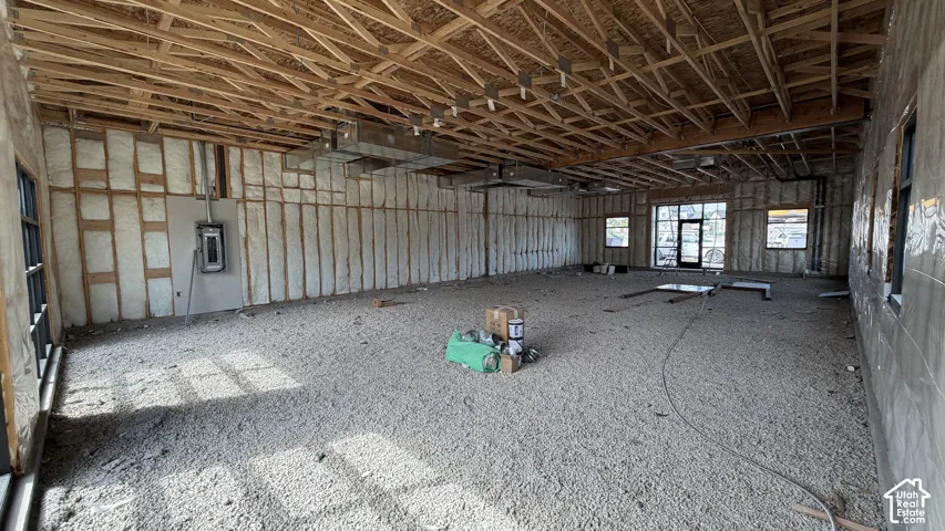 Exposed wood ceiling joists, insulated wall framing, multiple windows, and a glass-paneled entry door