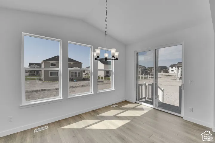 Vaulted ceiling, wood-finish flooring, multiple large windows, modern five-light chandelier, and a sliding glass door